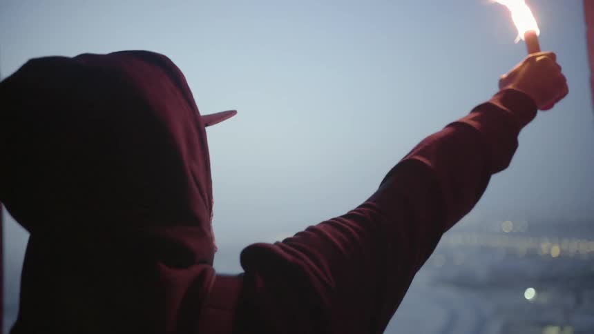 A person lights a flair and raises it to the sky