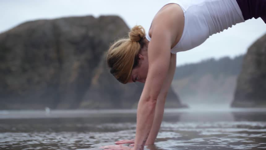 A white woman practices yoga on a wet beach
