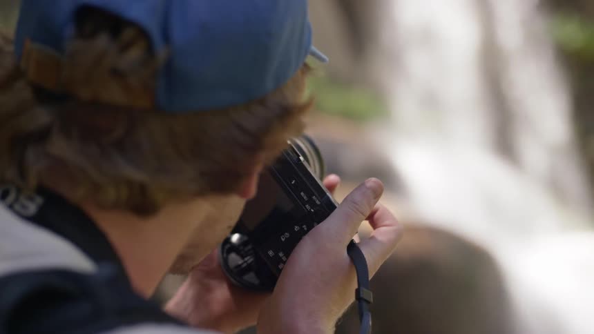 A man with a blue baseball cap and a camera taking pictures of a waterfall