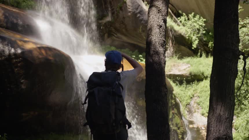 Male photographer takes a picture of the waterfall in the forest