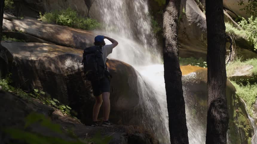 A man stops to look at a waterfall during a hike through the woods