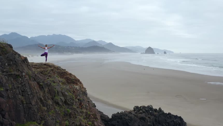 A woman does yoga on a cliff on the beach