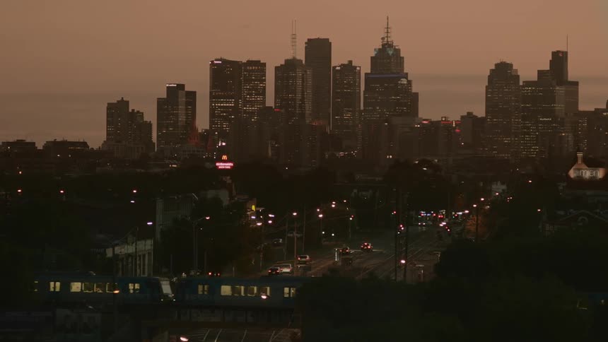 View of a city skyline behind traffic and a commuter train during sunset