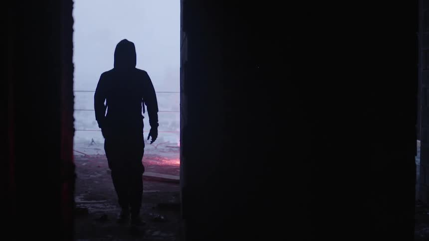 A man in a hood throws a flare on the ground and walks away