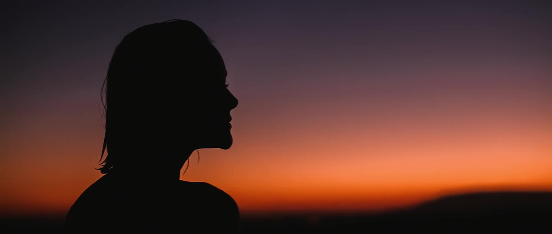 A woman with wet hair looks toward a sunset