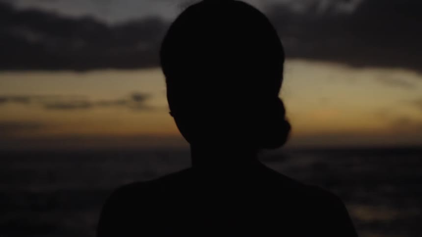 A silhouette of a woman standing on the beach looking at the sunset