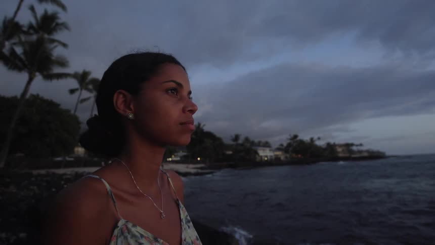 Woman stands on beach after dusk staring toward the sea