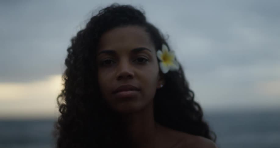 A black woman with a flower in her hair stands outdoors