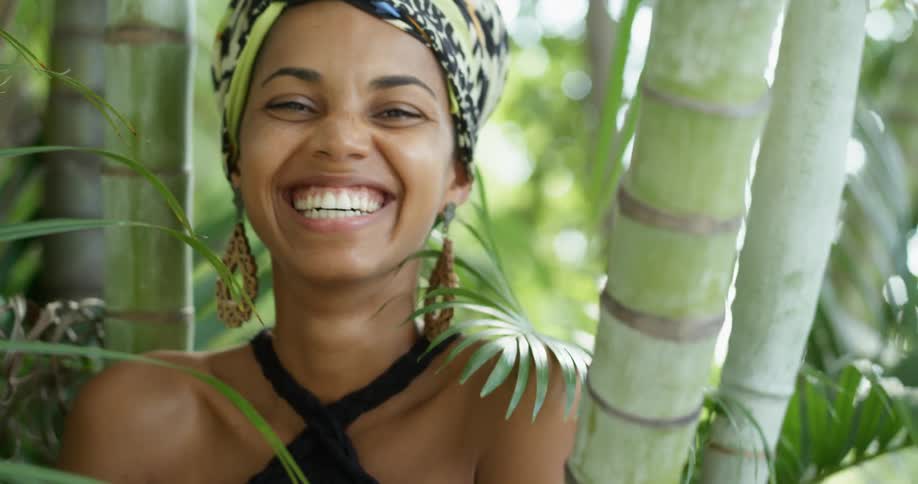 A young black woman stands in a grove of trees and laughs