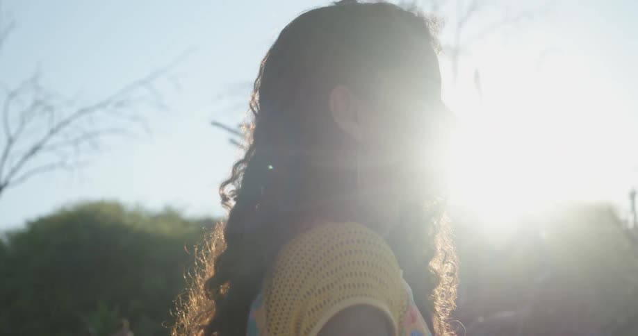 Woman stands outdoors as sun clears the tree tops