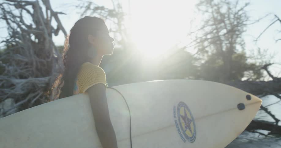 Brunette girl holding a surfboard walks to the sea in the late afternoon