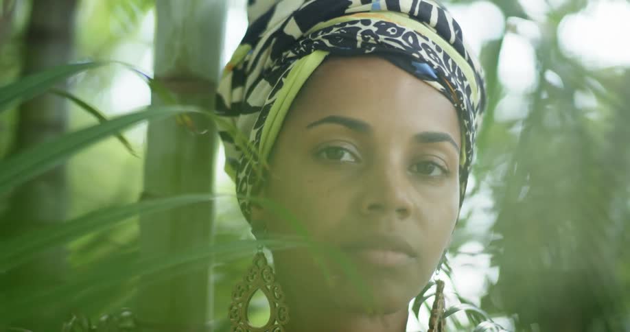 A woman with a head wrap and large earrings sits amongst bamboo