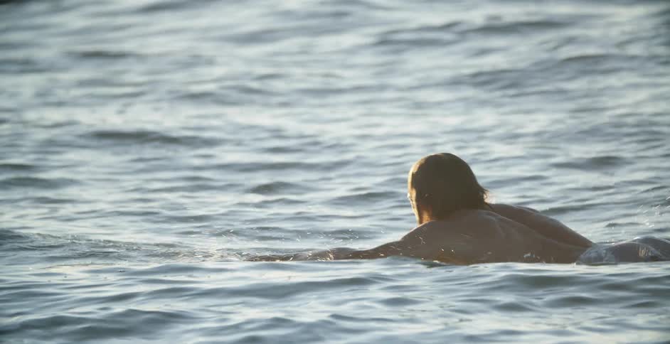 Man swims on a surfboard in the sea late afternoon