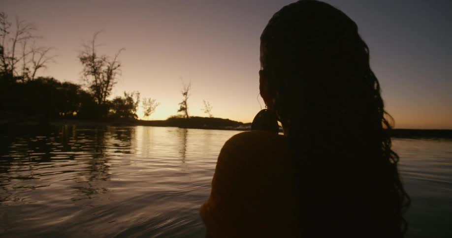 A woman stands up in the water at sunset