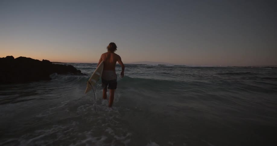 A man holding a surfboard runs into the ocean