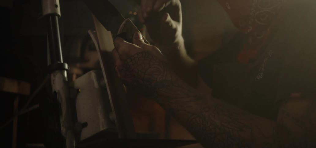 A man runs the handle of a knife over a machine as he shapes it
