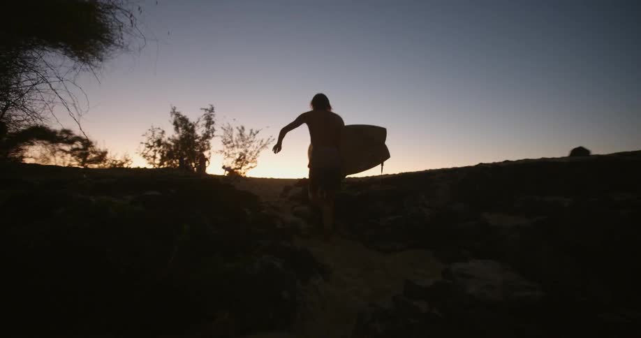 Man runs onto beach carrying surfboard at sunset