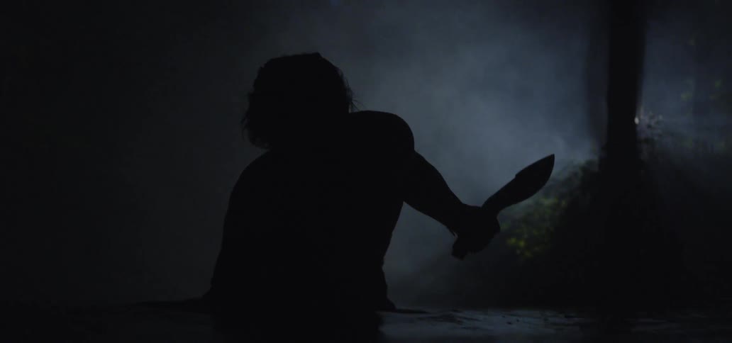 A man walking water in a dark cave while carrying a knife