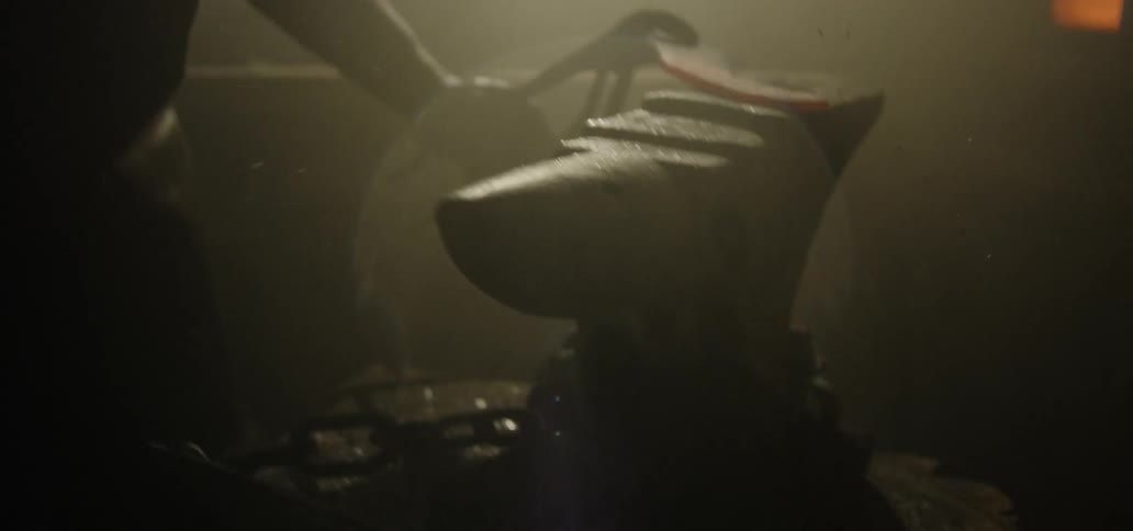 A man holding a blacksmith hammer strikes a piece of metal that he is holding on an anvil with large pliers