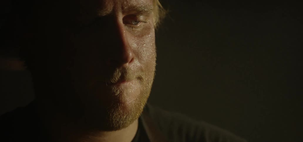 A man with sweat on his face focuses on his task in a darkened room