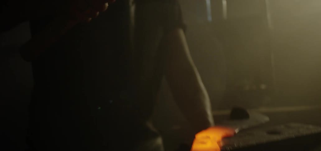 Blacksmith hammers glowing metal on anvil