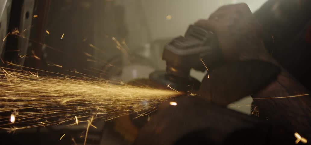 A tattooed man uses a grinding wheel on a piece of metal