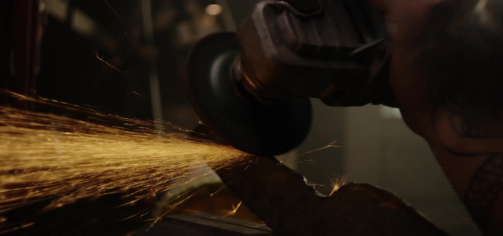 A man using an angle grinder on the tang of a blade