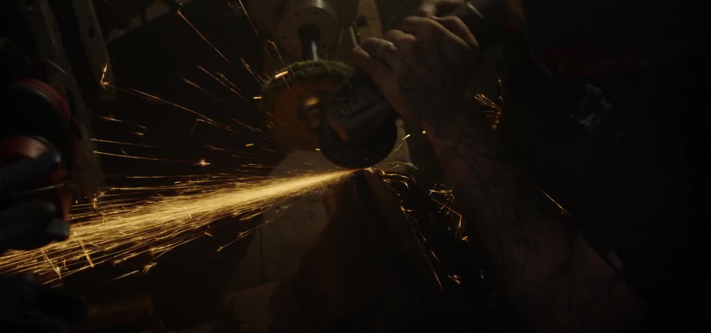 A blacksmith uses a grinding wheel on a piece of forged steel