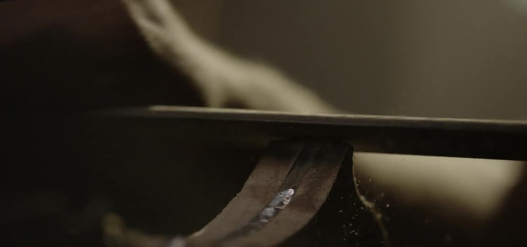 Sawdust flies as a man uses a file to sand and smooth a wooden knife handle