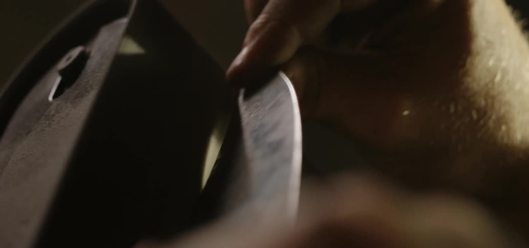 Man with tattoo sharpens the knife in the workplace