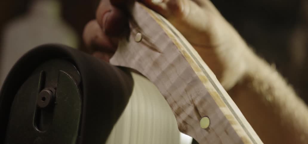 A man sands and smooths the wooden handle of a knife he made