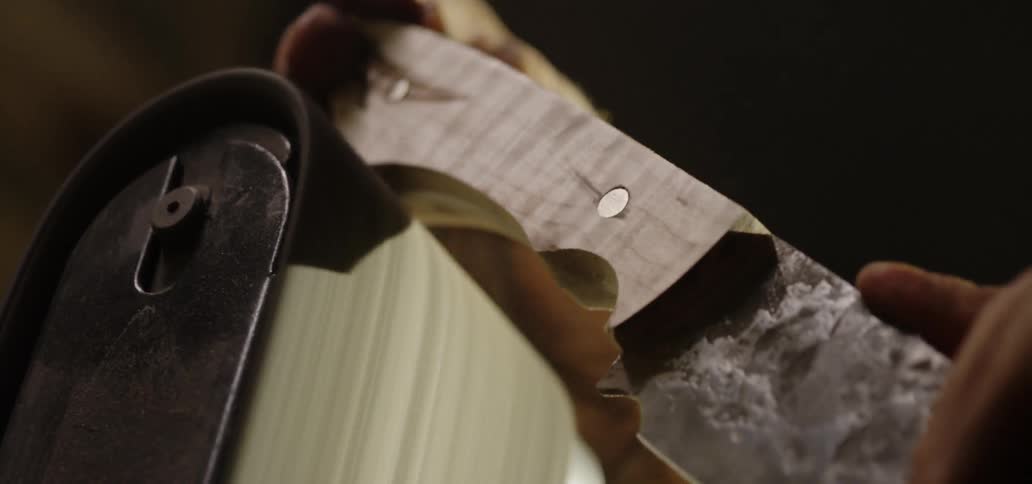 A person using electric sander to sand a knife handle