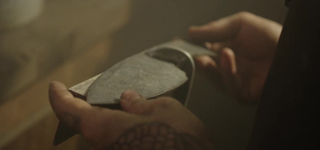 A person with tattoos on their hands holding a piece of metal