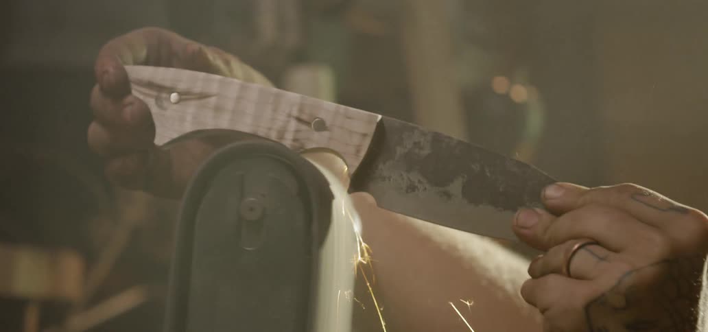 A man sanding the wooden handle of a knife with a power sander