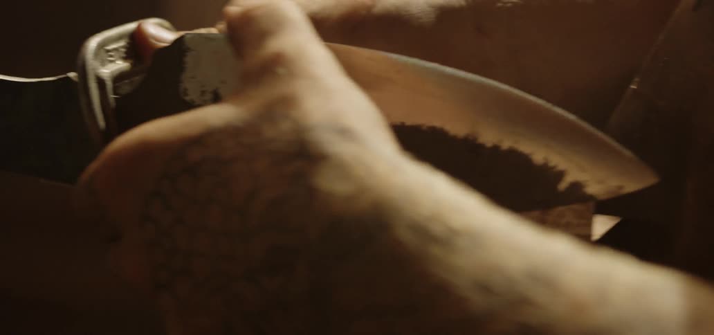 A white man rubs the blade of a knife with his thumb