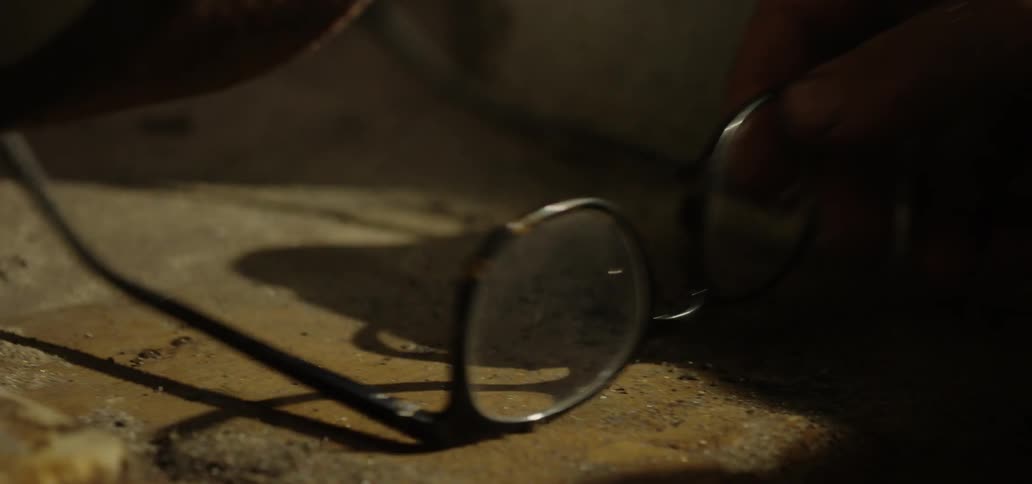 Person picks up eyeglasses from dusty surface
