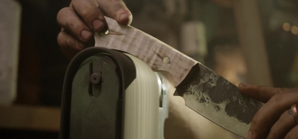 A person using an electric sander to sand a knife handle