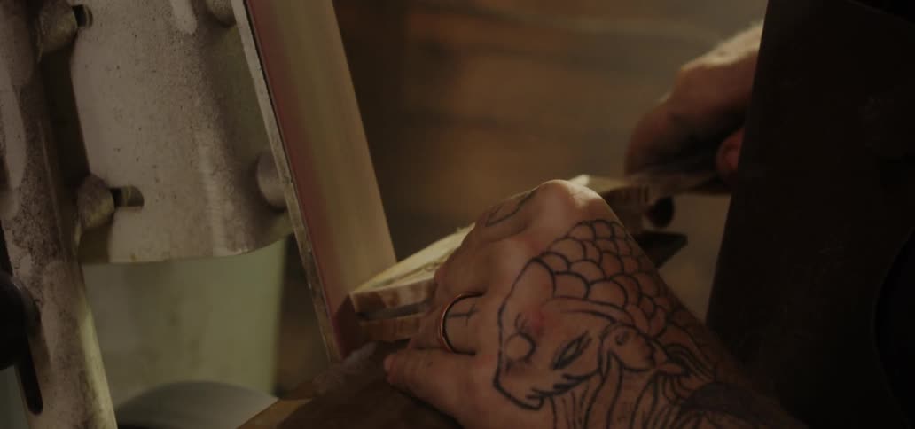 A man is shaping the handle of a knife on a belt sander