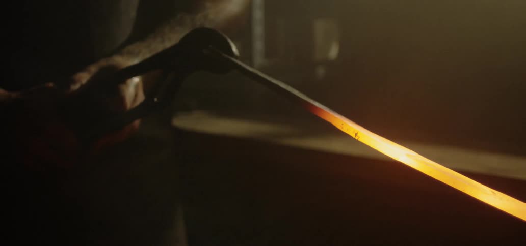 A blacksmith moves a red hot heated piece of metal with tongs