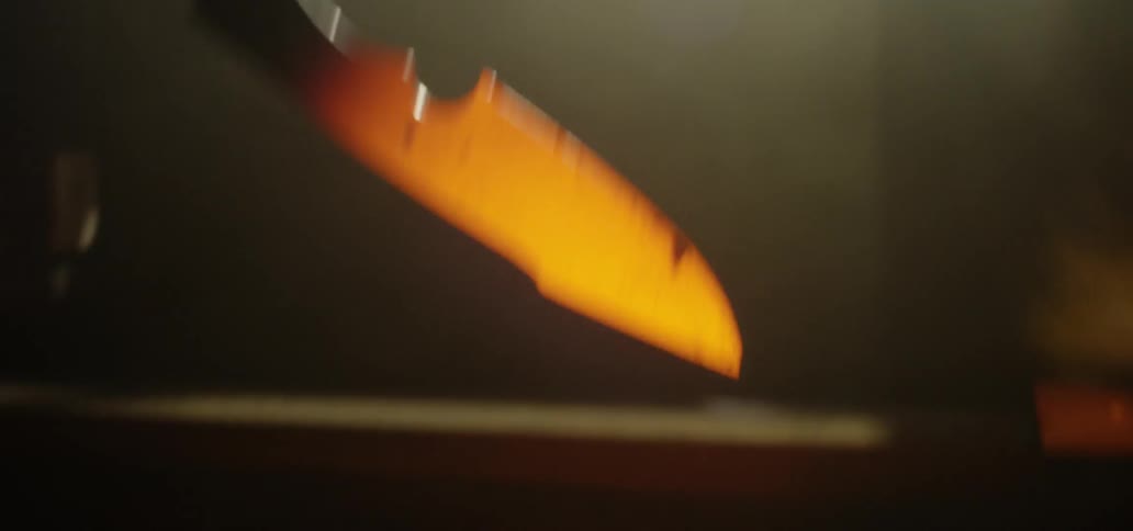 A person removes a red hot metal blade from a metalworking furnace