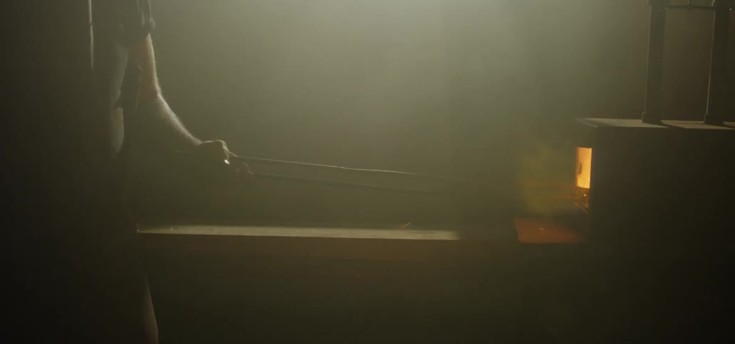 A man is pushing tongs into a blacksmith oven