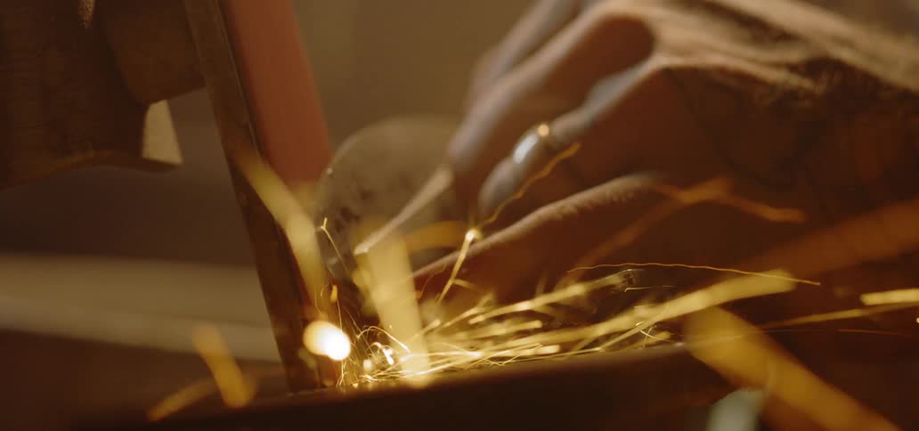 A worker sharpens a blade as sparks fly