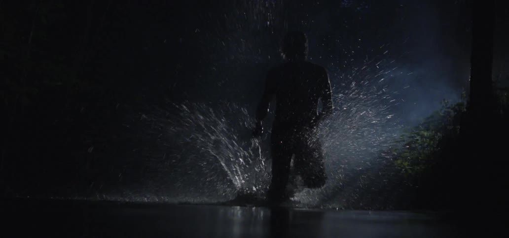 A man carrying a knife splashes as he runs through water at night