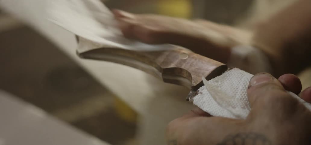 A man wiping down the wooden handle of a knife with a paper towel
