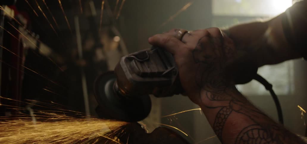 Male hands with tattoos grinding a muffler in a workshop