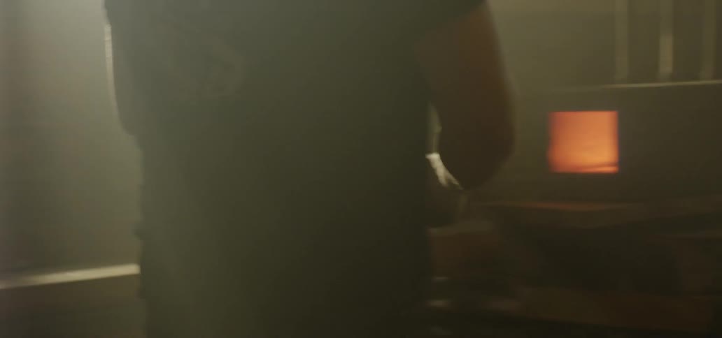 A man uses a tool to lift a piece of hot metal to a table