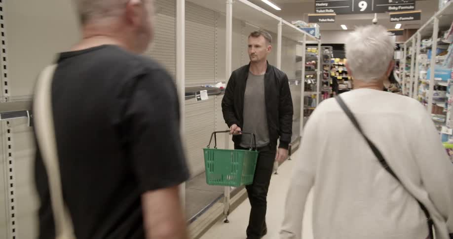A man walking through a shopping aisle where one side is completely out of stock