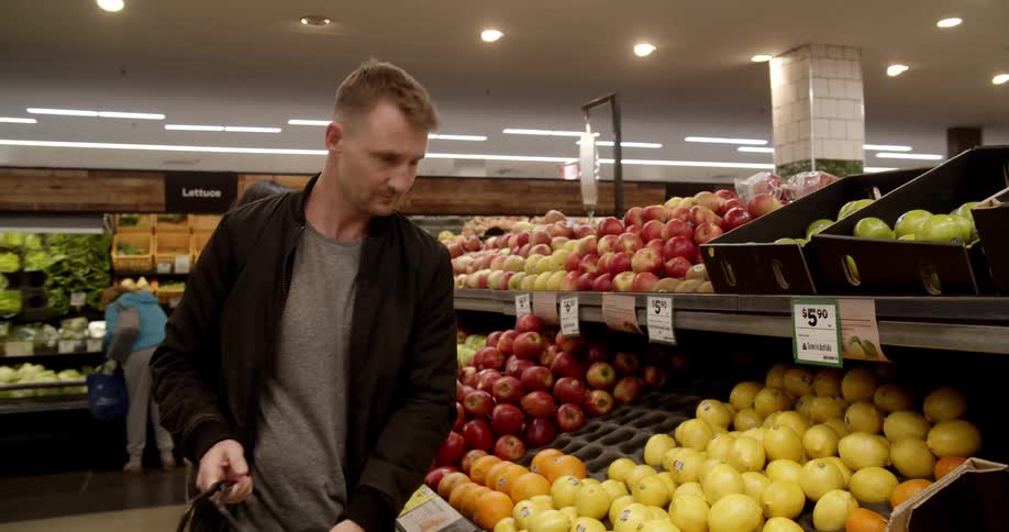 A man grabbing a pair of lemons from a shelf and putting them in a shopping basket