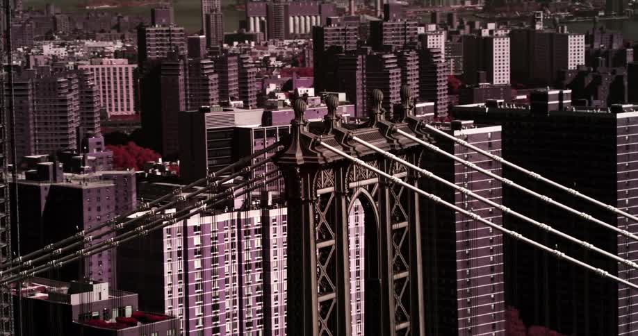 Close up of a suspension bridge in front of skyscrapers
