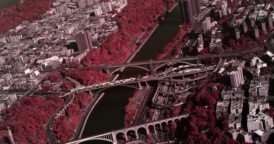 A busy city skyline with bridges over a river surrounded by buildings and trees